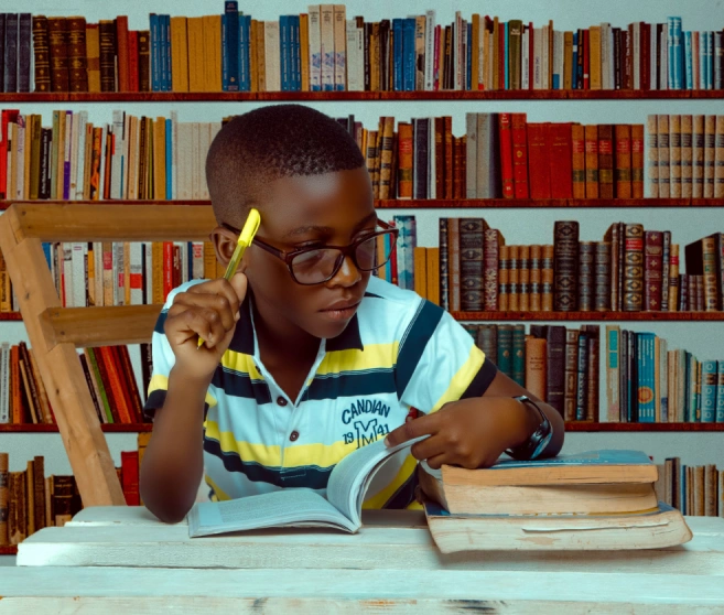 Young boy studying intently with books and pencil in a library.