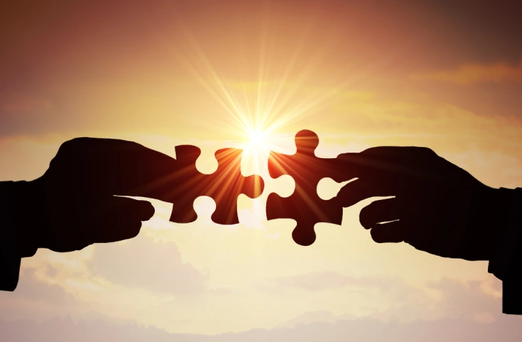 Two hands connecting puzzle pieces at sunset.